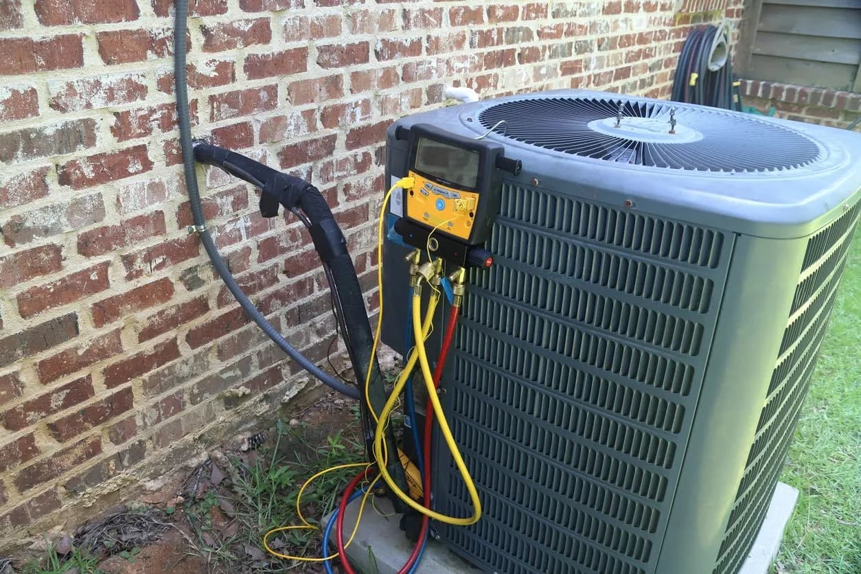 Technician's manifold gauges connected to an outdoor AC unit during a refrigerant check